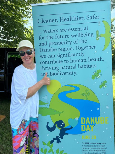 Woman (Susanne Brandstetter) stand with Danube Day roll-up. 