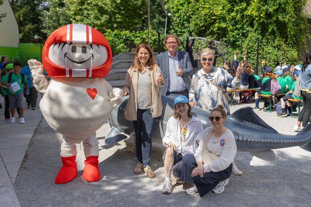 Five people and a mascot stand together outside. 