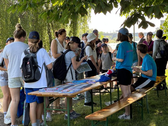 Children and adults stand around a table with pamphlets and information about Danube Day and the BMLUK. 