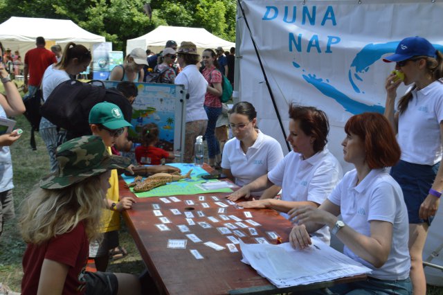 Children sit opposite women at a table, engaging in educational activities with fish cards.