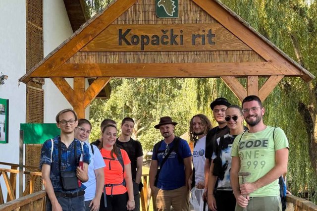 Several people gather outside under a wooden sign. 