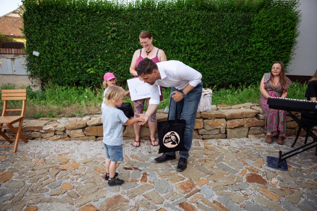 A man in a white shirt bends down to shake hands with a young child during an outdoor community event.