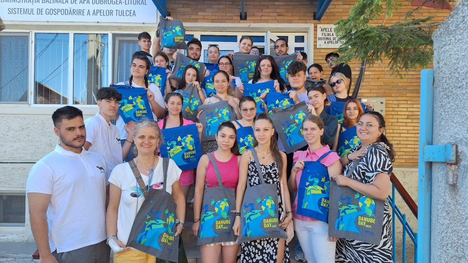 A group of young students gather outside with grey Danube Day 2025 tote bags. 
